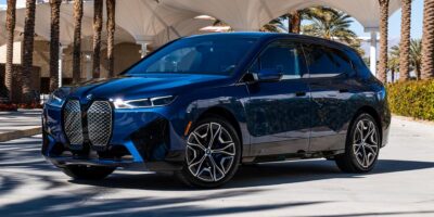 Luxury electric SUV in blue, showcasing the sleek design of the BMW iX range parked in a sunny palm tree-lined setting