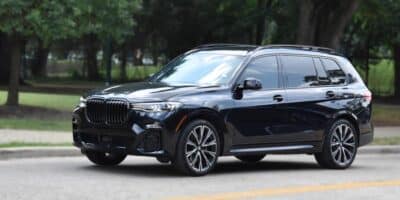 A black BMW X5 drive down an empty street with a forest of trees in the background.