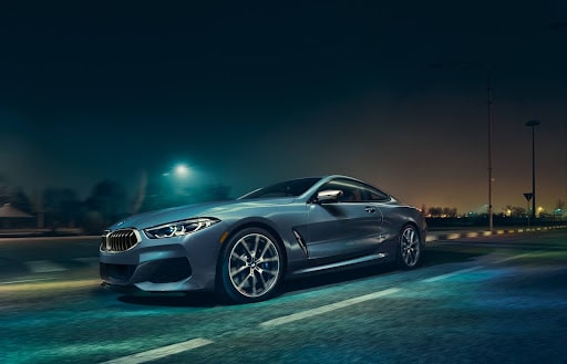 A light blue BMW under the night sky driving down the road.