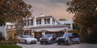 A holiday-themed scene with a BMW X3 M40i parked in front of a beautifully decorated home, accompanied by other BMW models, under a festive evening sky.