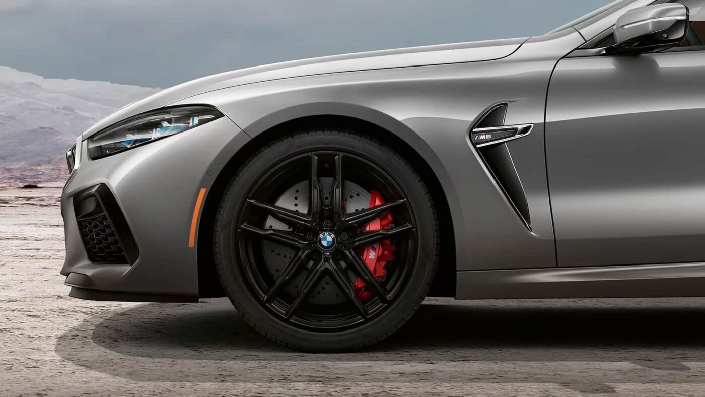 Close-up of 2025 BMW M8 Competition front wheel, featuring black alloy rims and red M-branded calipers.