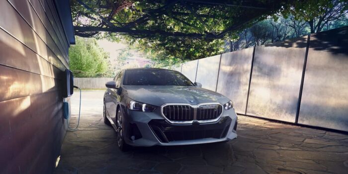 BMW i5 M60 electric vehicle parked in a serene outdoor setting, connected to a charging station.