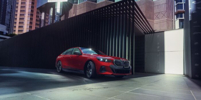 BMW i5 M60 in vibrant red parked in an urban setting, emphasizing its dynamic stance.