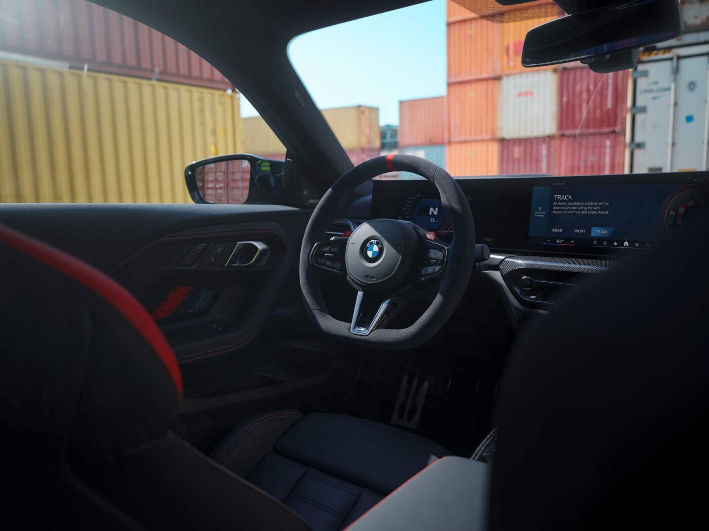 The driver-focused cockpit of the 2025 BMW M2, featuring a sporty steering wheel, BMW iDrive 8.5 infotainment system, and digital instrument cluster.