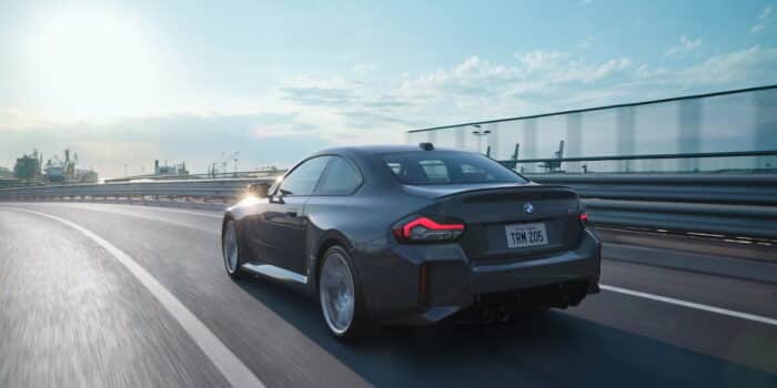 The 2025 BMW M2 in motion on a highway, showcasing its aggressive rear design, quad exhaust, and performance-driven aerodynamics.