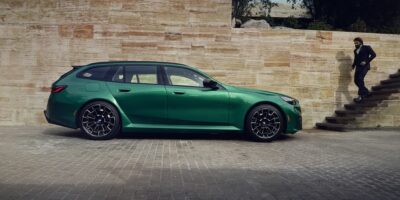 Green BMW M5 Competition parked beside stone wall with man in suit approaching, highlighting 2025 bmw m5 competition design and styling.