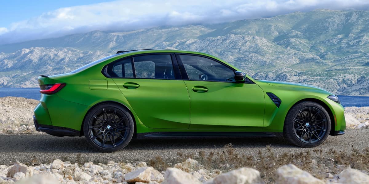 Side profile of bright green BMW M3 parked on scenic mountain road showing sporty design and aggressive stance.